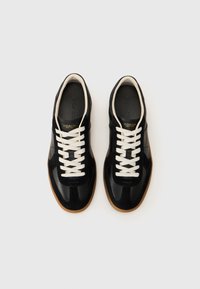 Black leather and suede sneakers with white laces and gum sole. Features branding on the insole and a sleek, modern design.