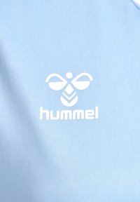Logo d'abeille blanche Hummel et texte sur un fond de tissu bleu clair texturé.