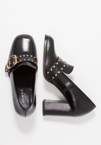 Chaussures à talons carrés en cuir noir avec un bout carré, dotées d'une large sangle ornée d'ét studs métalliques et d'une boucle dorée.