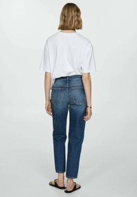 Weißes, übergroßes T-Shirt kombiniert mit hochgeschnittenen, dunkelblauen Jeans, die klassische Gesäßtaschen und einen umgeschlagenen Saum aufweisen. Schwarze Sandalen.