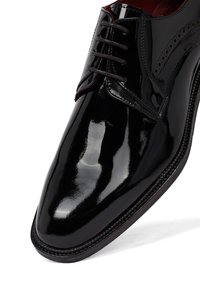 Zwarte gepolijste leren dresschoenen met veters en brogue-details, schuin gepositioneerd om de neus en zijkant te tonen.