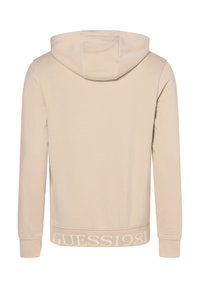 Felpa beige realizzata in morbido tessuto, con cappuccio regolabile, maniche lunghe e bordi a costine, caratterizzata dal logo "GUESS1981" in un colore a contrasto.