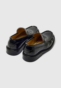 Sorte skinn slip-on sko med rund tå, elastiske detaljer og en teksturert såle. Glatt overdel med en subtil glans.