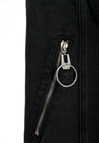 Chaqueta de mezclilla negra con un zipper plateado y una pestaña circular, que presenta una textura suave y un diseño limpio.