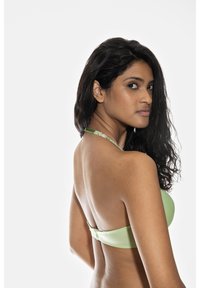 Vihreä halterneck-uimapuku, jossa on sileä pinta ja kukkakoristelu hihnassa, näyttää nykäisyn takaa ja lievää kaartumista vyötäröllä.