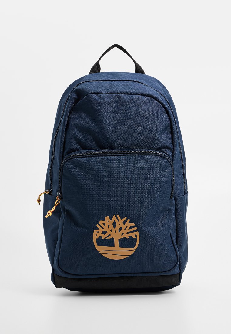 Sac à dos bleu marine en tissu texturé, avec poche avant et un grand logo d'arbre doré. Il dispose d'une base noire et d'une poignée de transport en haut.