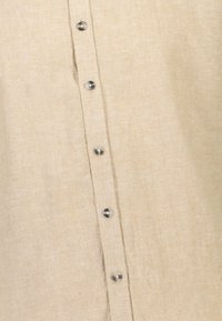 Beige linnen shirt met een gladde textuur, voorzien van zeven zilveren knopen aan de voorkant en een ontspannen pasvorm.