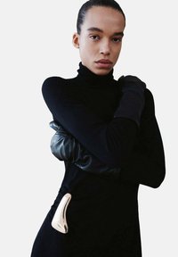 Robe à col roulé noire avec un accent métallique argenté sur le côté, associée à de longs gants en cuir noir. Texture lisse.