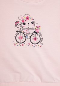 Vaaleanpunainen collegepaita, jossa on sarjakuvamainen kani ja kissa pyörän päällä, ympärillä värikkäitä kukkia ja "hauskaa hauskaa!" -teksti.