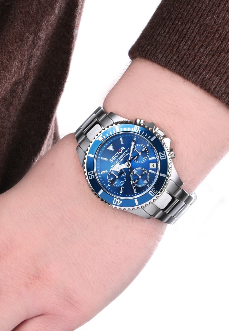 Orologio da polso con bracciale in argento, dotato di un quadrante blu, contrassegnato da indici delle ore bianchi e subquadranti, caratterizzato da una lunetta blu texturizzata e da una cassa in acciaio inox.