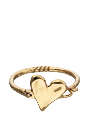 Bracelet en métal doré avec un grand pendentif en forme de cœur asymétrique et un détail côtelé sur le bracelet.