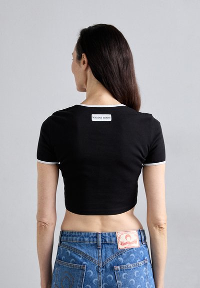 Črna skrajšana majica s belim obrobom, na hrbtni strani pa ima oznako logotipa. V kombinaciji z modrimi jeans hlačami z vzorčastimi žepe in logotipom.