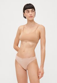 Hudenfarget bh og bikini-sett laget av glatt stoff; har justerbare stropper, minimalistisk design og en liten sløyfedetalj på bikinien.