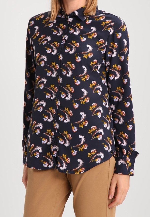 Granatowa bluzka zapinana na guziki z kwiatowym wzorem w kolorze różowym, białym i żółtym. Wykonana z gładkiego materiału, z długimi rękawami i spiczastym kołnierzykiem.