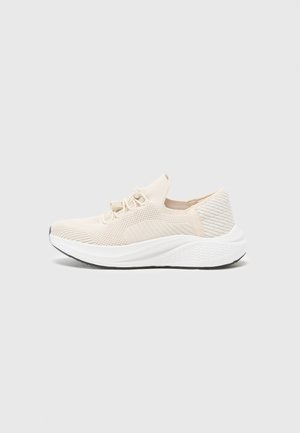 Beige neulotut slip-on-tossut valkoisella pehmustetulla pohjalla, teksturoidulla kantapäällä ja joustavilla nauhoilla helppoon pukemiseen ja mukavuuteen.