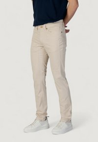 Pantalones ajustados beige con una textura suave, que presentan cinco bolsillos, costuras sutiles y un cierre de botón, combinados con zapatillas blancas.