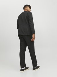 Black suit jacket with a slim fit, paired with matching trousers. The model wears black sneakers, showcasing a clean, modern look.