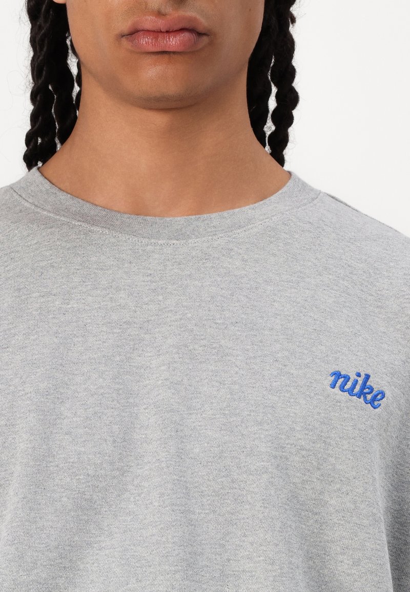 Felpa grigia in cotone con collo a giro e logo "nike" ricamato blu sul lato sinistro del petto. Tessuto morbido e vestibilità ampia.