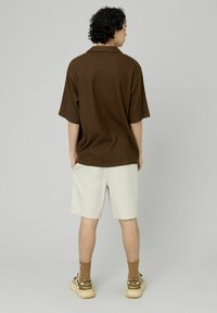 Chemise marron à manches courtes en tissu texturé, assortie à un short beige clair et rehaussée de chaussettes marron et de chaussures à motifs.