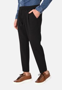 Pantaloni sportivi neri con vita regolabile, tasche laterali e vestibilità affusolata. Abbinati a sneaker marroni con lacci e a una camicia di denim.