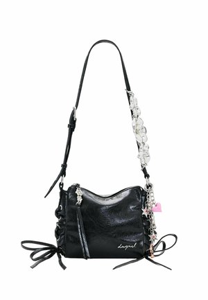 Bolso de hombro de piel negra con correa ajustable, detalles de lazos laterales, colgantes florales plateados, llaveros con forma de estrella y corazón, y cierre con cremallera.