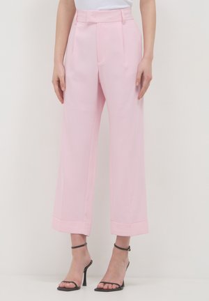 Woman wearing light pink high-waisted wide-leg pants and black strappy high-heeled sandals standing against a plain background.