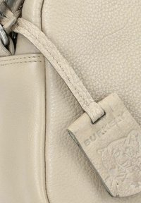 Bolso de mano de cuero beige con superficie texturizada, que presenta una correa y una etiqueta grabada con "BURKELY" y un diseño de gato.