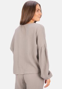 Grau gestrickter Pullover mit Waffelstruktur und lockerer Passform, der lange Ärmel und einen Rundhalsausschnitt besitzt. Die Rückseite zeigt ein sauberes, schlichtes Design.