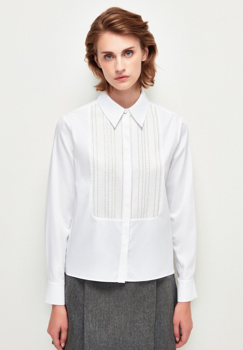 Witte blouse met lange mouwen en een met knopen sluitende kraag, voorzien van getextureerde verticale plooien aan de voorkant en een gladde stof overal.