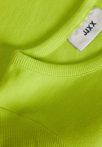 Close-up of a lime green ribbed fabric shirt neckline with a white tag featuring the brand name JJJXX in dark blue letters.