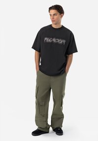 Tricou negru cu mânecă scurtă, având un mare logo grafic gri, asortat cu pantaloni cargo verzi măslinii, care au multiple buzunare și o croială relaxată.
