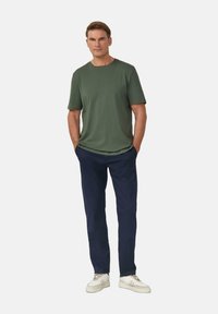 Zielona koszulka z krótkim rękawem, granatowe spodnie i białe sneakersy. Casualowy krój z gładkiego materiału i prostymi nogawkami. Brak widocznych wzorów lub akcentów.