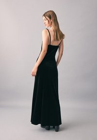 Černé maxi sametové šaty s tenkými ramínky, přiléhavým živůtkem a splývavou sukní. Hladká textura a minimalistický design s odhalenými zády.