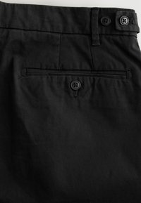 Pantalon en coton noir à la texture lisse, doté de deux boutons noirs à la taille et d'une poche arrière avec une fermeture à bouton.