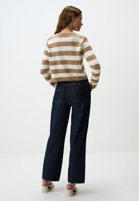 Gestreepte trui in beige en crèmekleurige brei, gecombineerd met high-waisted donkere denim wijde pijpen jeans, met achterzakken en subtiele stiksels.