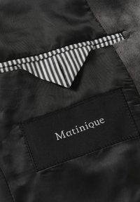 Melnas satīna audums ar svītrotu iekšējo kabatu. Uz plakana melna birkas ir izšūts uzraksts "Matinique".