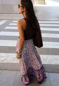 Maxirock mit floralem Muster in Rosa und Lila, kombiniert mit einem dunklen Tanktop. Accessoires sind mehrere silberne Armreifen und Sonnenbrillen.