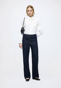 White long-sleeve blouse with textured puff sleeves, paired with dark denim straight leg pants and a small black shoulder bag.
