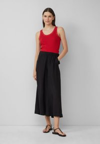 Rode geribbelde tanktop met kantafwerking, gecombineerd met zwarte wijde broek met elastische tailleband en zijzakken, en zwarte platte sandalen.