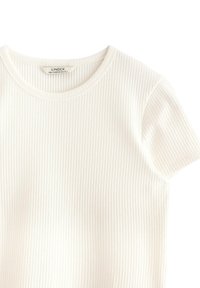 Vit ribbad T-shirt med rund halsringning och korta ärmar, tillverkad av ett mjukt, figurnära tyg. Lappen synlig inuti halsringningen.
