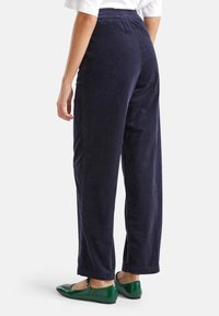 Person wearing navy blue corduroy wide-leg pants with elastic waist and green Mary Jane flats, standing against a white background.