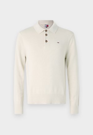 Ilgas rankovės kremas megztinis su polo apykakle, trimis rudiem mygtukais ir mažuoju logotipu. Megztas tekstūra ir nertomis rankovių bei apatinėmis kraštinėmis.