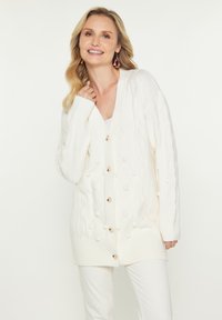 Großer Strick-weißer Cardigan mit V-Ausschnitt, ausgestattet mit einem Rautenmuster und Bobble-Akzenten, verschlossen mit Holzknöpfen.