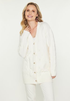 Großer Strick-weißer Cardigan mit V-Ausschnitt, ausgestattet mit einem Rautenmuster und Bobble-Akzenten, verschlossen mit Holzknöpfen.
