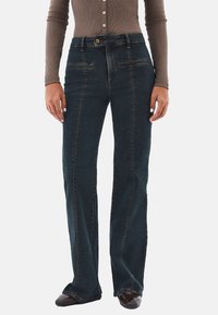 Jeans de mezclilla azul oscuro con un diseño de pierna recta, costuras naranjas, bolsillos frontales y un cierre de botón en la cintura.