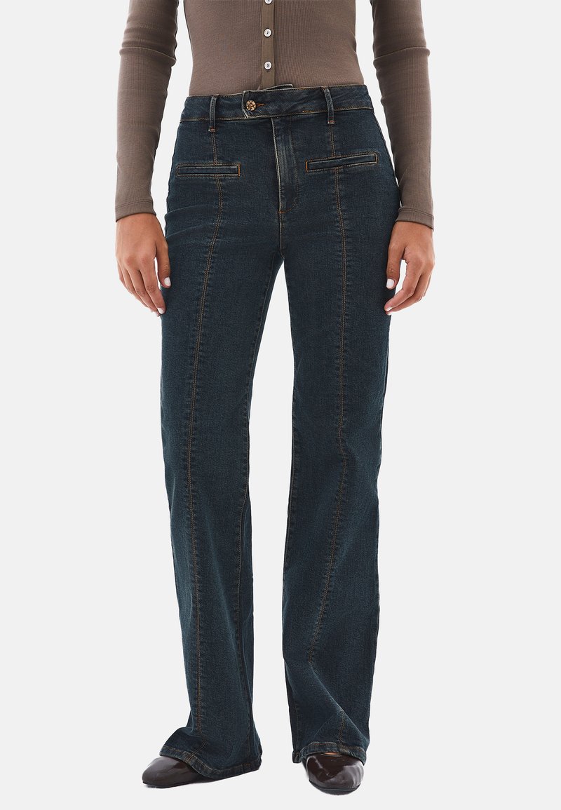 Jeans de mezclilla azul oscuro con un diseño de pierna recta, costuras naranjas, bolsillos frontales y un cierre de botón en la cintura.