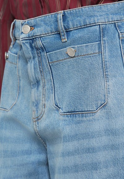 Lys blå denimbukser med høy midje, kontrasterende oransje sømmer, to frontlommer og en baklomme med rund form.