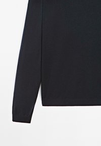 Chemise noire à manches longues en tissu lisse et doux. Présente un ourlet droit et des poignets ajustés sans motifs ni décorations visibles.