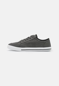 Sneaker in tela grigia con profilo basso, punta rotonda, lacci sulla parte anteriore e due strisce orizzontali nere sulla suola in gomma bianca.