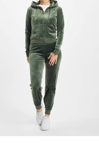 Grön velour träningsdräkt med en zip-up huva och framfickor samt matchande byxor; båda har ribbade ärmslut och en mjuk, slät yta.